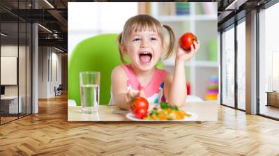 happy child eats dinner and shows tomatoes Wall mural