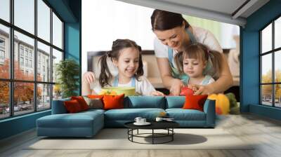 Happy mother and her daughters enjoy making healthy meal together at their home Wall mural