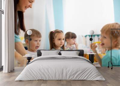 Kids and carer together eat fruits and vegetables in kindergarten or daycare Wall mural