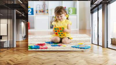 Little girl child playing with lots of colorful plastic digits or numbers indoors. Wall mural