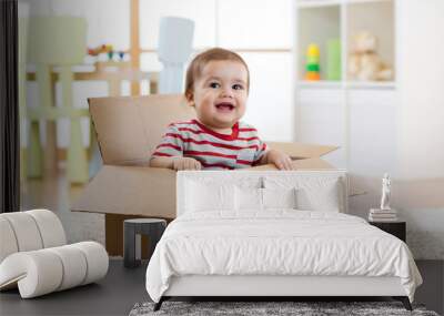 Smiling baby boy sitting inside cardboard box after moving to a new apartment Wall mural