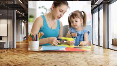 Teacher helping child girl to work with colored paper Wall mural