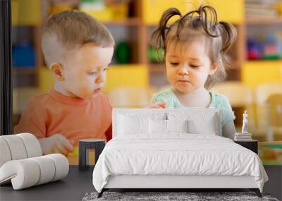 Toddlers boy and girl playing at table with educational toys. Children infants in creche or daycare. Wall mural