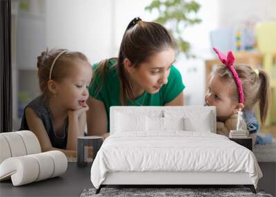 Young mother reading a book to her kids daughters. Children and mom lying on rug in cozy living room. Wall mural