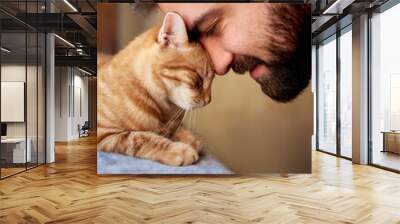 Muzzle of a red cat and a man's face. Close-up of handsome young beard man and tabby cat - two profiles. Pets and humans friendship, love and trust concept Wall mural