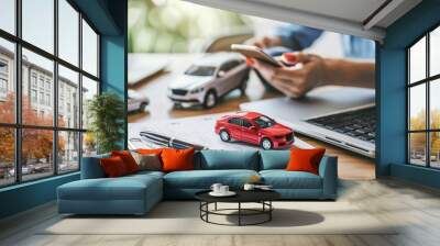 Person comparing car insurance rates using smartphone among model cars and paperwork. Online Car Insurance Comparison Concept Wall mural