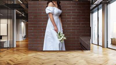 Portrait of American bride in white luxurious dress with bouquet of flowers against a brown brick wall. Wedding photo in retro style Wall mural