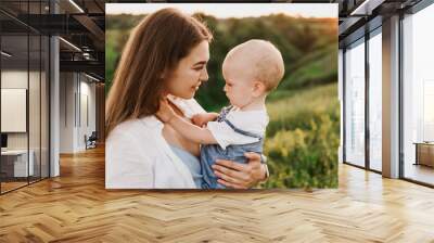 Young beautiful mother with her little daughter hug, kiss, laugh and walk in nature at sunset. Photo of a mother with a small child at sunset. Wall mural