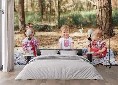 Kids in traditional ukrainian clothes play in forest in sunbeam. Boy and two girls. Wall mural