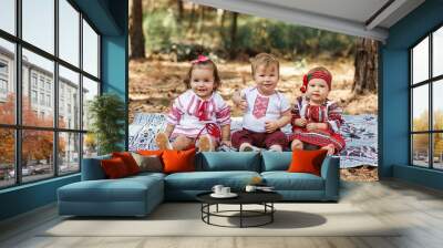 three children in traditional ukrainian shirts sits on ground in spring forest. Vyshyvanka style Wall mural