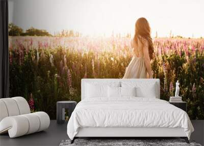 Young woman walking on flower field at sunset on background. Horizontal view with copy space Wall mural