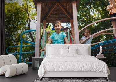 The little girl is sitting on a slide in the playground Wall mural