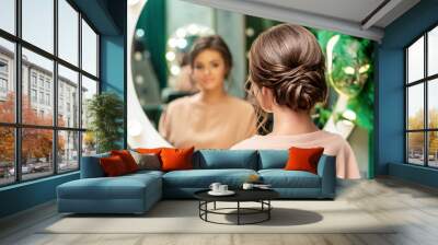 Beautiful young woman with hairstyle looking in the mirror at beauty salon. Wall mural