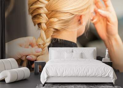 Braiding braid. Hands of female hairdresser braids long braid for a blonde woman in a hair salon Wall mural