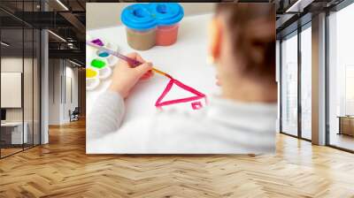 Child's hand with brush drawing the house on white paper by watercolors. Wall mural