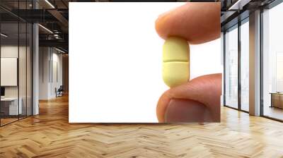 yellow and notched pill held between two fingers Wall mural