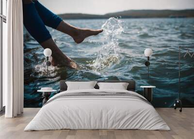 A happy young girl is kicking feet on a sea pier and splashing water Wall mural