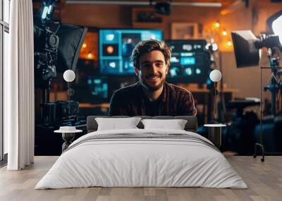 Male Vlogger in Professional Media Studio. Smiling young man sits at a desk surrounded by cameras and studio lights, recording content in a professional setting. Wall mural