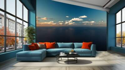  A vast expanse of blue water beneath a clear sky dotted with clouds, where a solitary plane traverses Wall mural