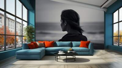  a woman standing on a beach looking out at the ocean in a black and white photo with the ocean in the back ground and the woman's head.  generative ai Wall mural