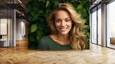  a woman with blonde hair smiling in front of a wall of green leaves with a white smile on her face. Wall mural