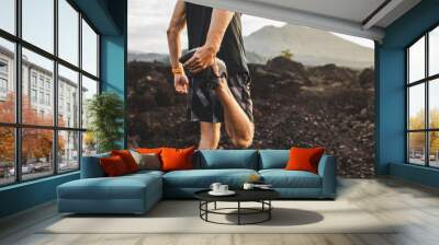 Runner stretching leg and feet and preparing for trail running outdoors. Active and healthy lifestyle concept. Mountain view on background. Wall mural