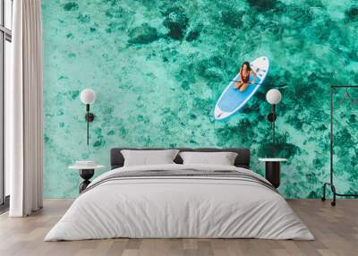 Woman sitting on sup board and enjoying turquoise transparent water and coral reef. Tropical travel, wanderlust and water activity concept. Wall mural