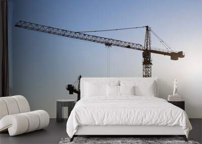 Construction cranes on blue sky and sunrise background. Housing construction in city Wall mural