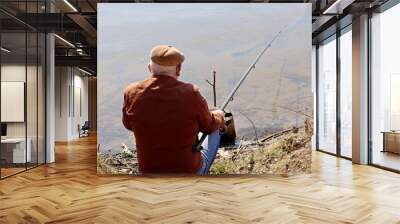 Fisherman sitting near the water with a fishing rod, rear view. Old man angling on the river coast at spring Wall mural