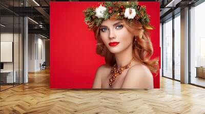 Portrait of beautiful young woman with Christmas wreath. Beautiful New Year and Christmas tree holiday hairstyle and makeup. Beauty girl portrait isolated on red background. Colorful makeup and hair Wall mural