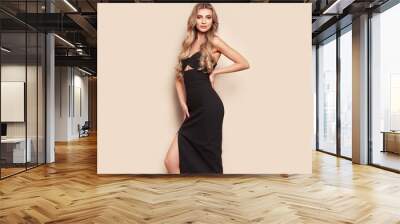 Portrait of gorgeous elegant sensual blonde woman wearing fashion black dress isolated on beige background. Model woman with long curly hairstyle. Care and beauty hair product Wall mural