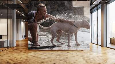 Woman with white Dogo Argentino dog puppy taking shower on the beach Wall mural