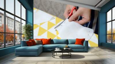 Women's hands cut the fabric with scissors according to the pattern on the table. Wall mural