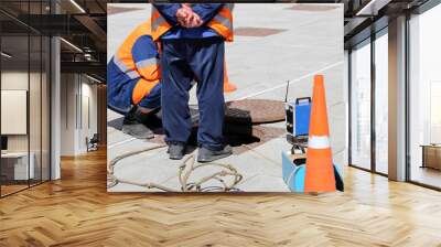 Workers over the open sewer hatch on a street. Concept of repair of sewage, underground utilities, water supply system, cable laying, water pipe accident Wall mural