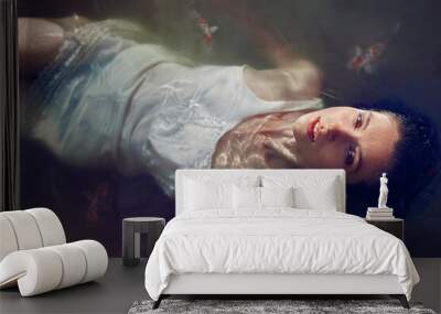 Beautiful young woman in white dress lying in the water with fishes. High angle view Wall mural