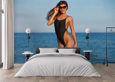 Sexy beautiful woman in black little bikini on sea background. Exotic model at the beach. Tanned ideal skin and fit sporty figure. No cellulite, healthy lifestyle and tropical tourism concept Wall mural