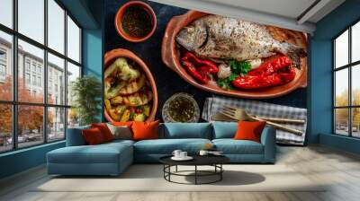 Delicious baked dorado fish with spices in a clay plate and fried vegetables, closeup, top view Wall mural