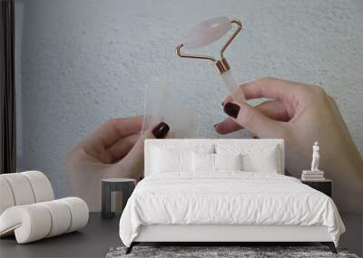 Pink jade roller and gua sha massager in the hands of a young girl on a light background Wall mural