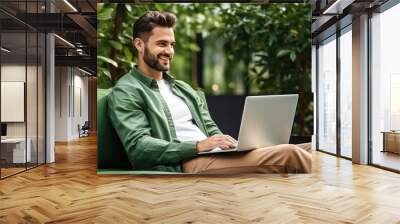 Cheerful man working on laptop seated on a green beanbag Wall mural