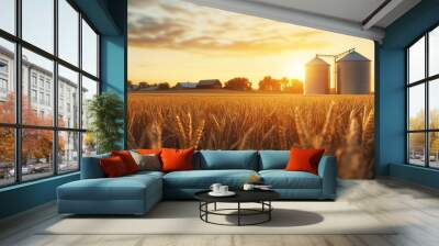 Golden wheat field with silos at sunset in rural farmland during harvest season Wall mural