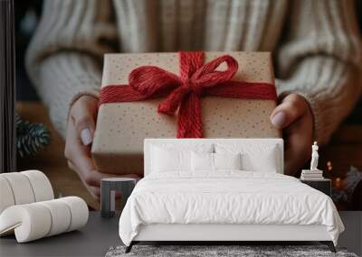 Person holding a beautifully wrapped gift with red ribbon amid festive decorations during winter Wall mural