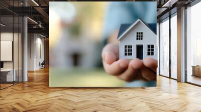 Person holds a wooden house model outdoors during daylight in a natural setting Wall mural