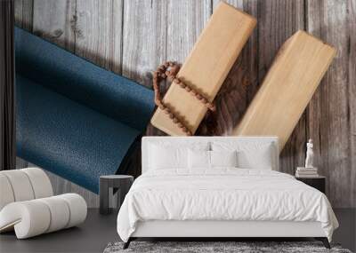 Closeup of two wooden yoga blocks, belt, rudraksha rosary and blue yoga mat on the wooden floor. Wall mural