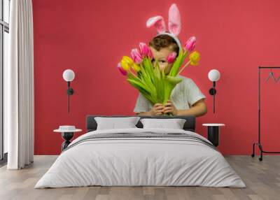 Happy Easter. A child in a rabbit costume holds a bouquet of yellow and pink tulips. A charming baby with funny bunny ears. Spring Easter holiday. The concept of a happy childhood. Wall mural