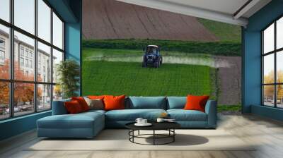 Aerial view of tractor spraying crop in green farm fields with pesticide Wall mural