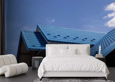 The roof of a house covered with sheets of blue metal tiles against the background of the sky on a summer day. Business selling building materials or repairing house roofs Wall mural