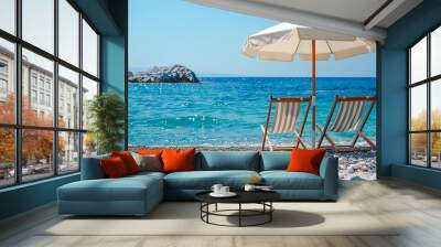 Two deckchairs under a white umbrella on a pebble beach. Vacation concept Wall mural