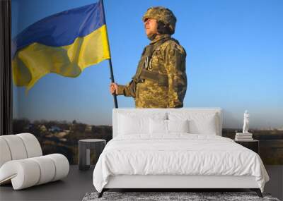 Portrait of soldier in military uniform lifted up flag of Ukraine in hill. Ukrainian army man holding waving flag. Victory against russian aggression. Invasion resistance concept. Slow motion Wall mural