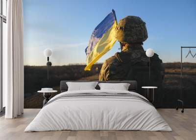 Ukrainian army soldier holding waving flag of Ukraine. Portrait of man in military uniform and helmet lifted up flag in hill. Victory against russian aggression. Invasion resistance concept. Slow mo Wall mural