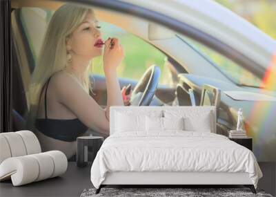 Woman applying makeup in the car. A beautiful blonde woman behind the wheel is applying makeup. Sunny, rainbow, glare Wall mural